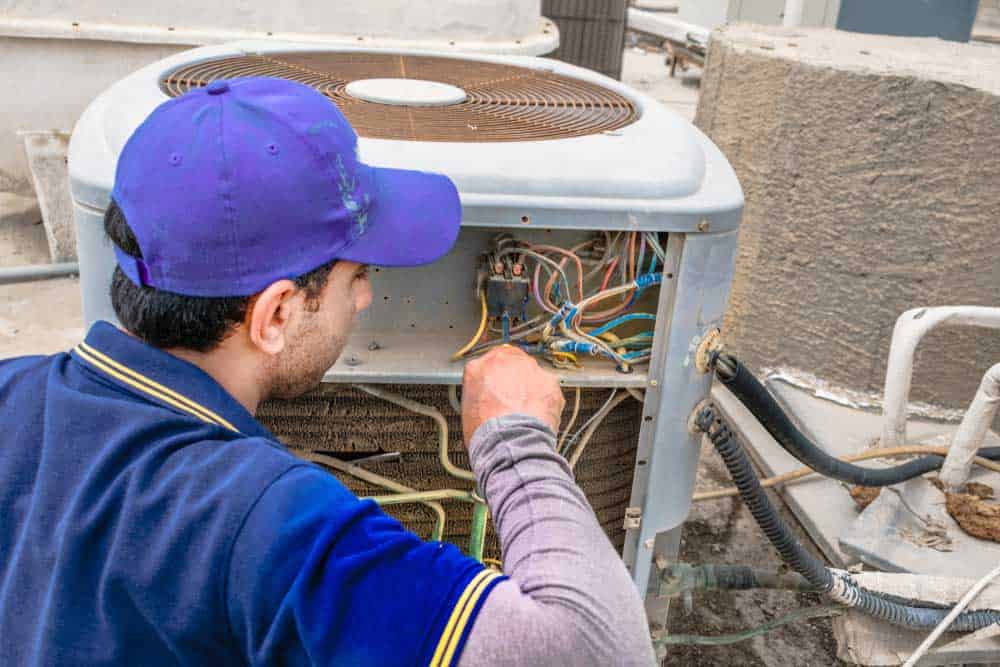 An electrician fixing a heavy air conditioning unit on the rooftop of a building