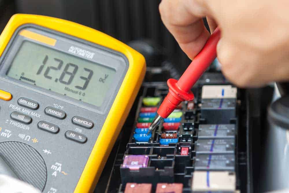 An electrician using a multimeter to test fuse voltages in a fuse box