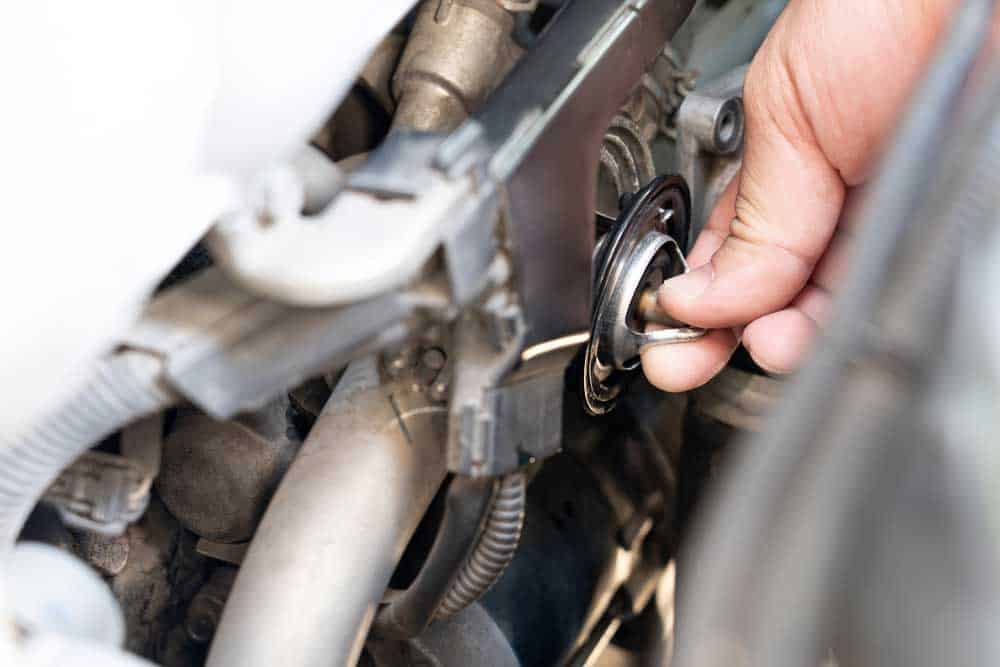 A professional mechanic with a car thermostat.