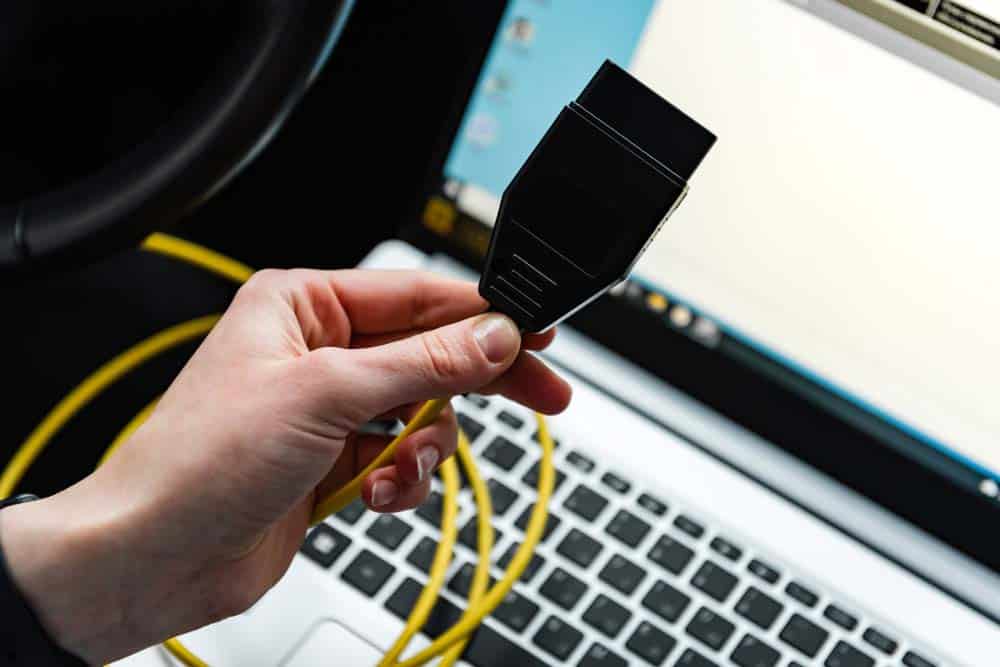 A person holding an OBD interface cable before connecting it to the vehicle’s port