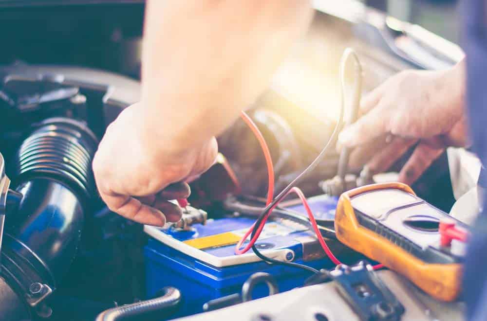 A mechanic measuring the voltage across a car battery’s terminals